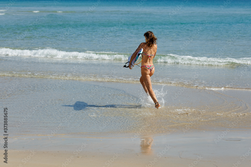 young beautiful girl in a swimsuit with a surfboard in her hands on the beach near the water, sea, summer, heat, sunny day, clear sea water, wave, lifestyle, sport, leisure, vacation, day off,