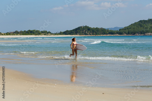 young beautiful girl in a swimsuit with a surfboard in her hands on the beach near the water  sea  summer  heat  sunny day  clear sea water  wave  lifestyle  sport  leisure  vacation  day off 