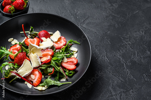 Healthy delicious salad with Camembert, strawberries, nuts, chard and arugula. Black background. Top view. Copy space
