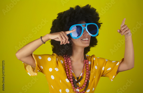 Young beautiful and smiling woman with curly afro hairstyle pointing and looking up, indicating direction with fingers.