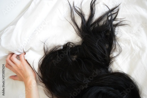 Close up sexy woman hand pulling and squeezing white sheets in ecstasy in bed. Orgasm on white bed. Sex and erotic concept. Long black hair on a white linen.
