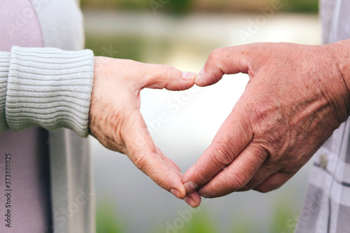 Relationship, love and seniors concept - close-up of senior couple showing hand heart gesture. Nature and lake background. © Alina