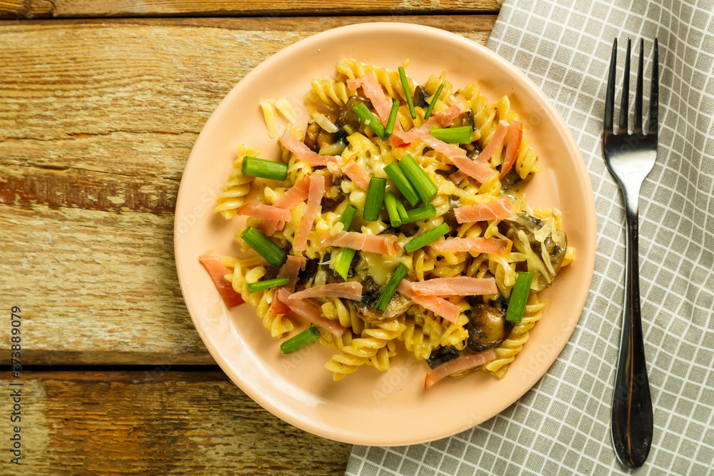 a plate of pasta with ham and mushrooms in a creamy sauce on the table with a fork on a napkin.