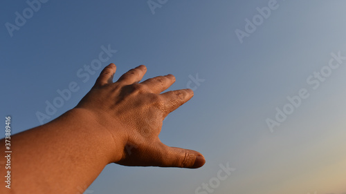 Frau mittleren Alters hält Hand in den Himmel, blauer Himmel als Hintergrund für Handrücken