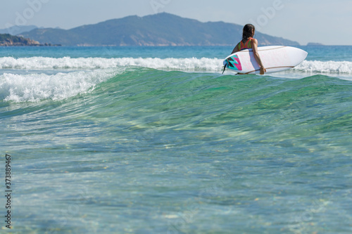 a girl with a surfboard enters the sea, summer, sunny day, clear water