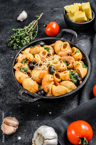 Conchiglie rigate pasta  puttanesca with anchovies, tomatoes, garlic and black olives. Black background. Top view