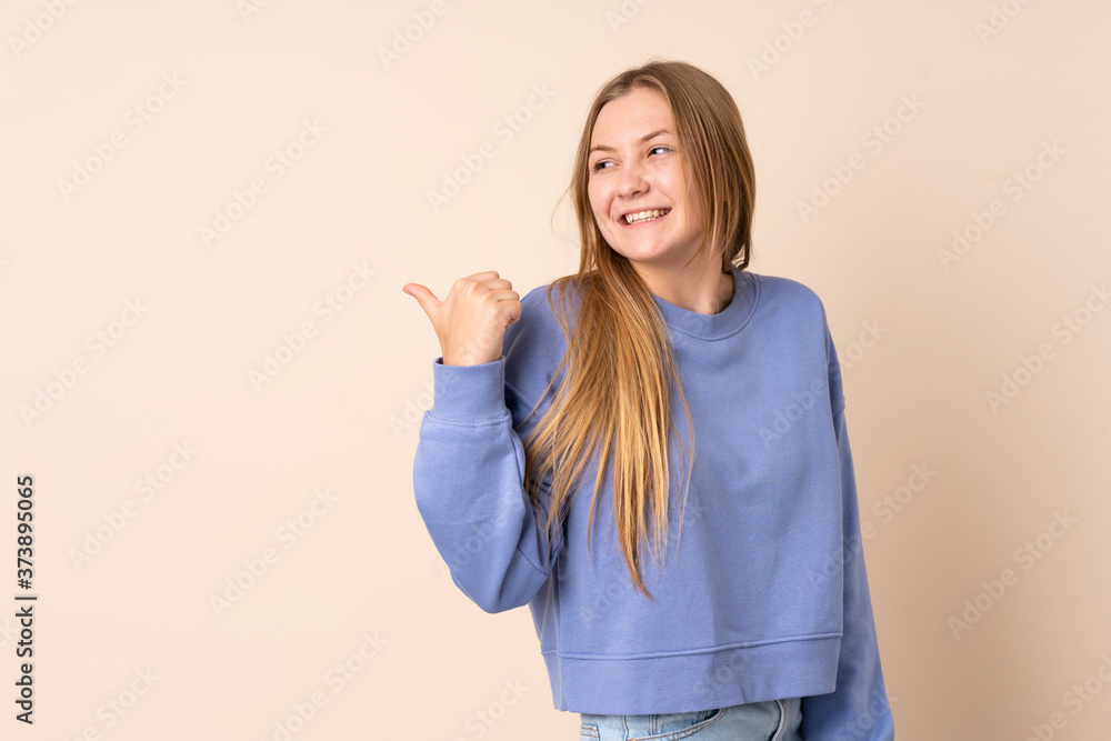 Teenager Ukrainian girl isolated on beige background pointing to the side to present a product Teenager Ukrainian girl isolated on beige background pointing to the side to present a product