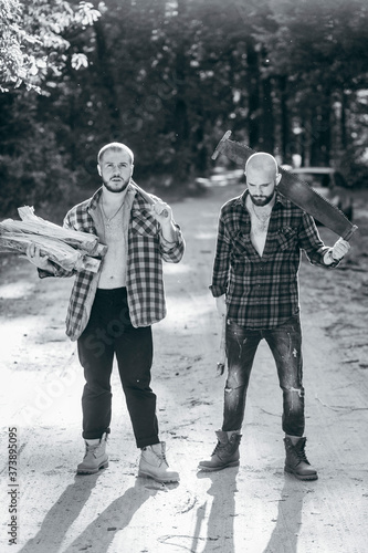 Two bearded brutal woodcutters with hand saw and axe