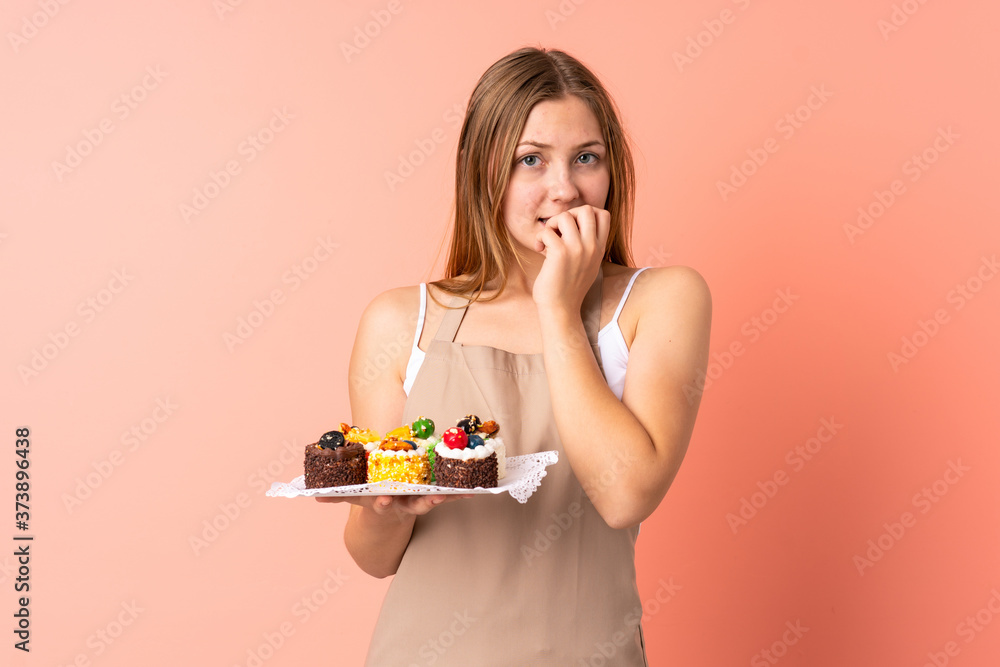Pastry Ukrainian chef holding a muffins isolated on pink background nervous and scared Pastry Ukrainian chef holding a muffins isolated on pink background nervous and scared