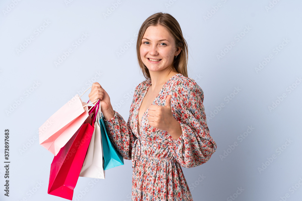 Teenager Ukrainian girl isolated on blue background holding shopping bags and with thumb up Teenager Ukrainian girl isolated on blue background holding shopping bags and with thumb up