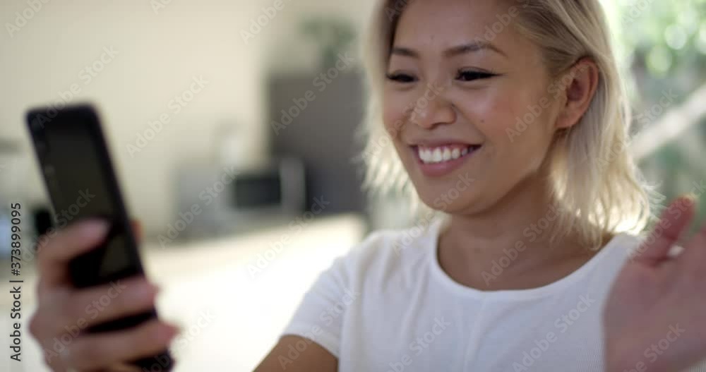 Young attractive asian woman with funky blonde hair speaks to her friend via a video call, happy to hear from her. Technology, young generation, connection Young attractive asian woman with funky blonde hair speaks to her friend via a video call, happy to hear from her. Technology, young generation, connection