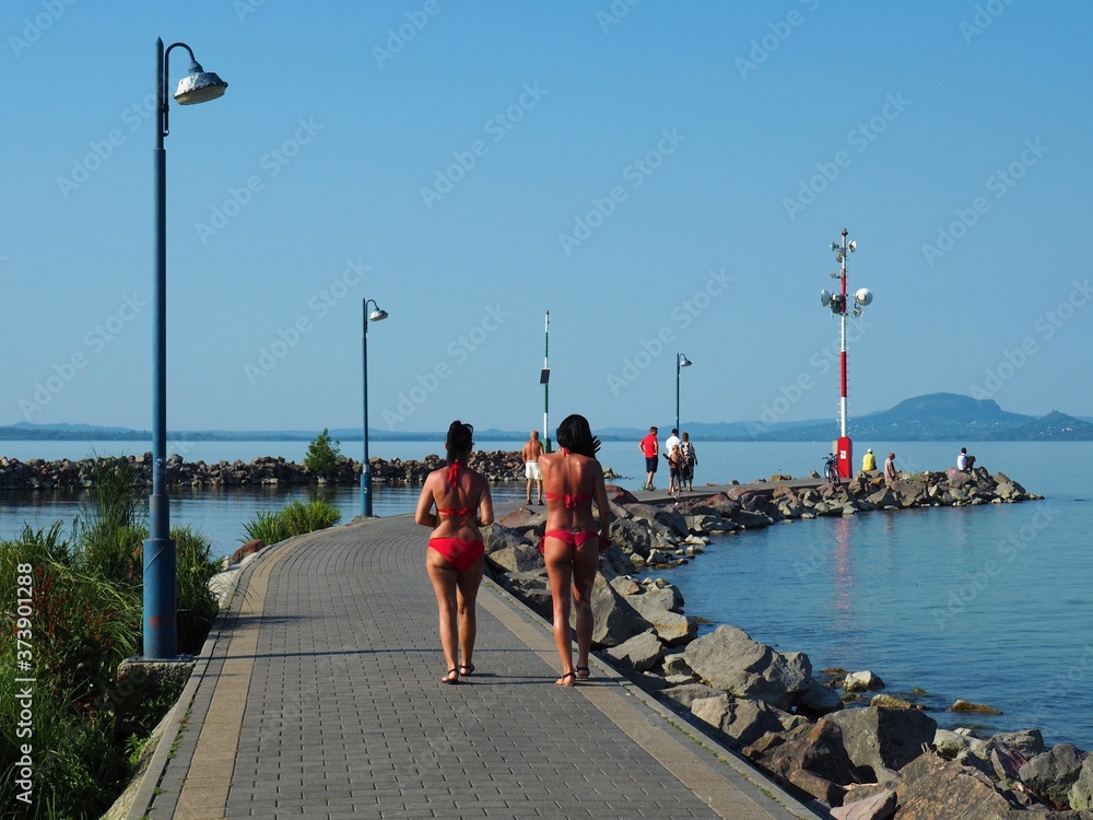 Obraz premium Balatonmáriafürdő, Hungary - July 30, 2020: Bronzed women in red bikinis walking on the pier at the lake Balaton in a hot summer day in Hungary