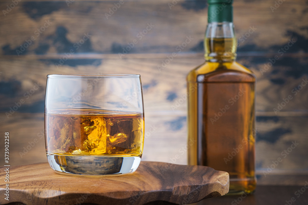 Golden whiskey witn ice cubes on wooden table with bourbon or scotch bottle Golden whiskey witn ice cubes on wooden table with bourbon or scotch bottle