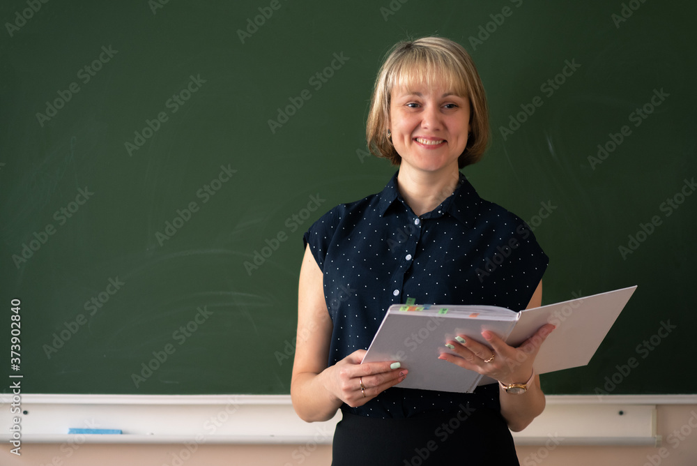 Smiling teacher with a class book on the school blackboard background. Smiling teacher with a class book on the school blackboard background.