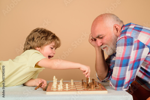 Playing chess. Kid playing chess with grandpa. Grandfather and grandson play chess. Family relationship. Grandfather and grandson. Moves in chess game.
