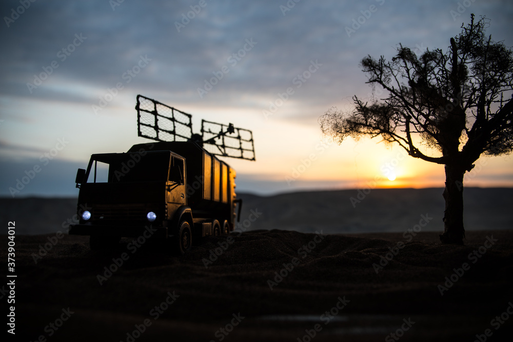 Obraz premium Silhouette of mobile air defence truck with radar antenna during sunset. Satellite dishes or radio antennas against evening sky.