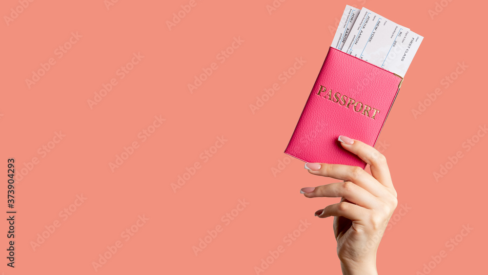 Passport control. Global immigration. Female hand holding foreign id in pink cover first class flight ticket isolated on coral copy space background. Vacation tour. Holiday trip. - obrazy, fototapety, plakaty 