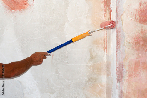 male hand with paint roller applies primer to the wall