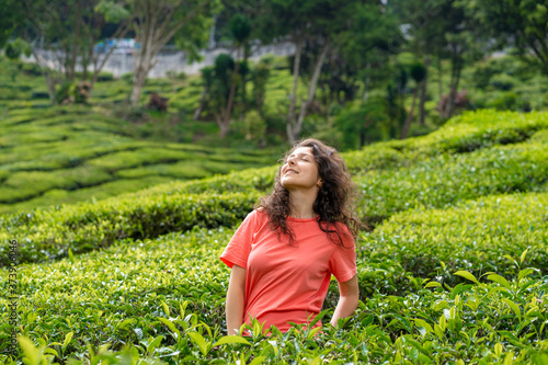 Beautiful brunette girl posing in the middle of the tea valley between green tea bushes.