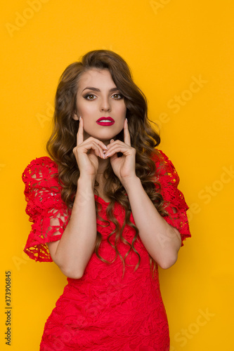 Beautiful Woman In Elegant Red Lace Dress Poses With Fingers On Chin