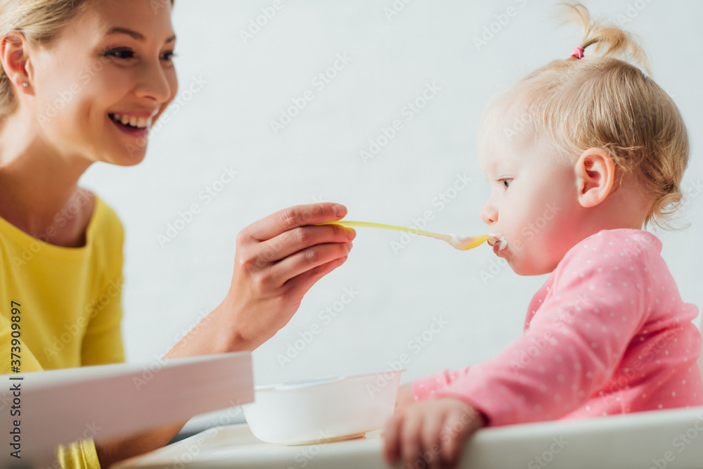 Selective focus of mother feeding daughter with baby food at home Selective focus of mother feeding daughter with baby food at home