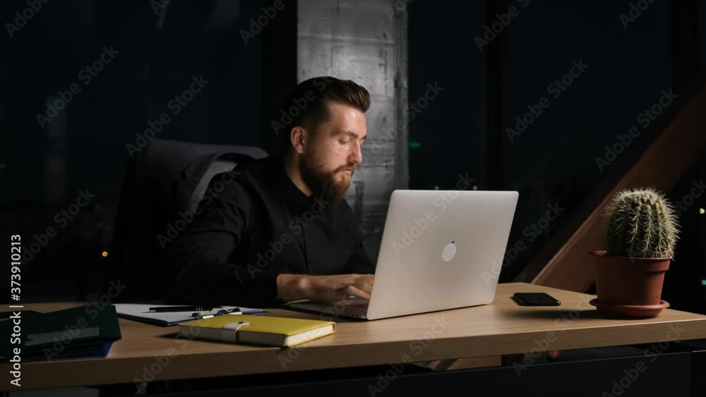 Bearded businessman that is working in a modern office at midnight is typing a letter and drinking a cup of coffee. Bearded businessman that is working in a modern office at midnight is typing a letter and drinking a cup of coffee.