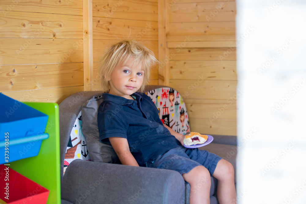Sweet toddler boy, playing in wooden doll house in garden Sweet toddler boy, playing in wooden doll house in garden