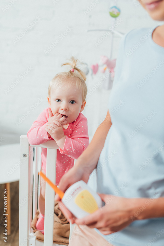 Selective focus of infant in crib near mother holding baby monitor Selective focus of infant in crib near mother holding baby monitor