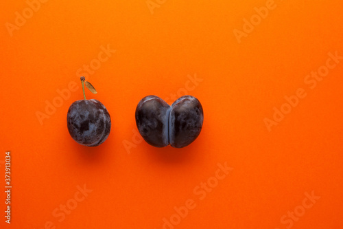 Ripe plum and ugly accreted prunes on an orange background. Place for text. Fused fruits. Funny, unnormal vegetable or food waste concept photo