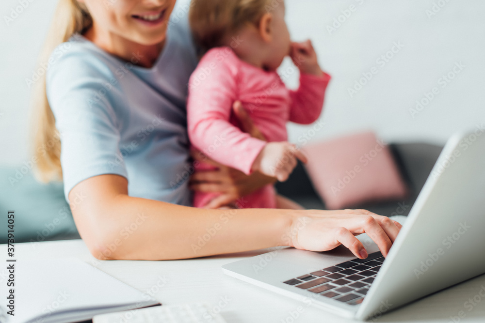 Selective focus of freelancer using laptop while holding baby daughter at home Selective focus of freelancer using laptop while holding baby daughter at home