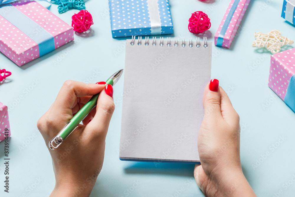 Top view of female hand making some notes in noteebok on blue background. New Year decorations and toys. Christmas time concept Top view of female hand making some notes in noteebok on blue background. New Year decorations and toys. Christmas time concept