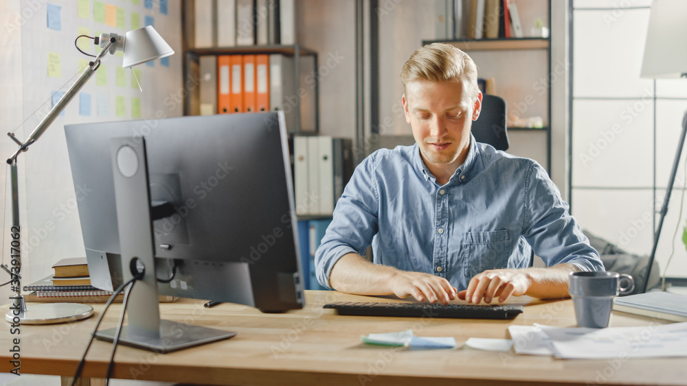 Creative Entrepreneur Sitting at His Desk Works on Desktop Computer in the Stylish Office. Handsome Young Businessman Uses Computer, Does Outsourcing Job, Designs New Apps and Develops Software Creative Entrepreneur Sitting at His Desk Works on Desktop Computer in the Stylish Office. Handsome Young Businessman Uses Computer, Does Outsourcing Job, Designs New Apps and Develops Software