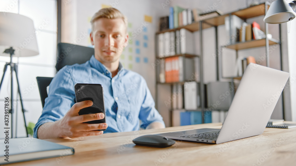 Businessman Sitting at His Desk Works on Desktop Computer in the Stylish Office, Picks up and Starts Using Smartphone, Uses Social Media App, Emailing Business Partners, Messaging Businessman Sitting at His Desk Works on Desktop Computer in the Stylish Office, Picks up and Starts Using Smartphone, Uses Social Media App, Emailing Business Partners, Messaging