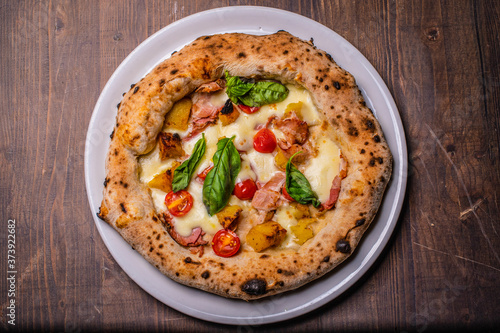 Pizza napoletana gourmet con basilico, patate al forno, pomodori, mozzarella e pancetta