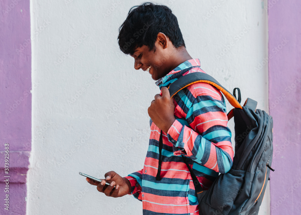 Portrait of an Indian kid wearing backpack using mobile phone and smiling