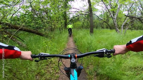 Two cyclists ride a forest trail on a cloudy day. Mountain bike. First-person view. FPV.