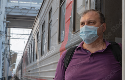 man in a medical mask near the train car. concept of travel during the pandemic.