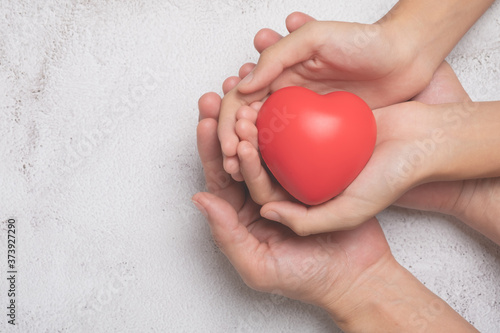 Fototapeta Naklejka Na Ścianę i Meble -  Hands holding a red heart on cement background, CSR or Corporate Social Responsibility, health care, family insurance, heart donate concept, world health day.