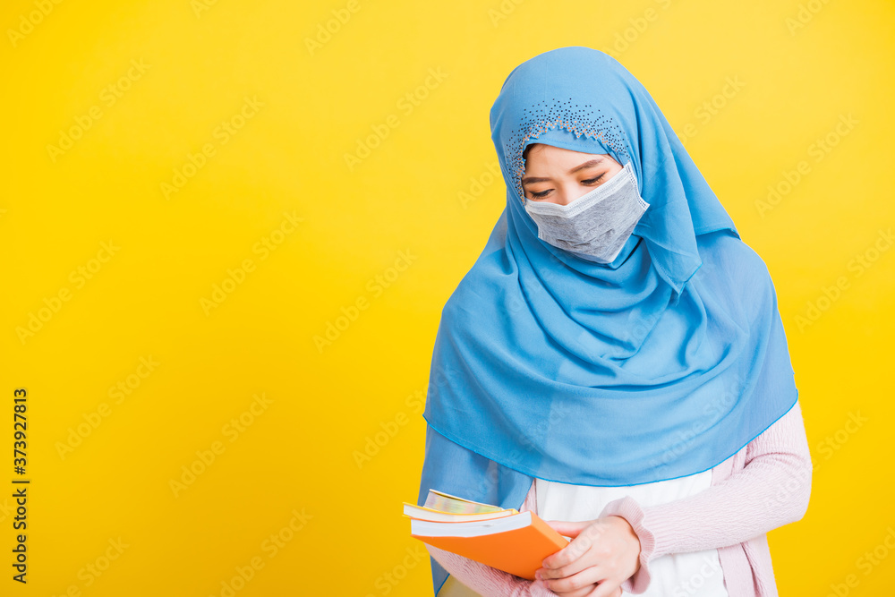 Asian Muslim Arab, Portrait of young woman religious wear veil hijab and face mask protective to prevent coronavirus she student hold books on hand, isolated on yellow background, Back to college Asian Muslim Arab, Portrait of young woman religious wear veil hijab and face mask protective to prevent coronavirus she student hold books on hand, isolated on yellow background, Back to college