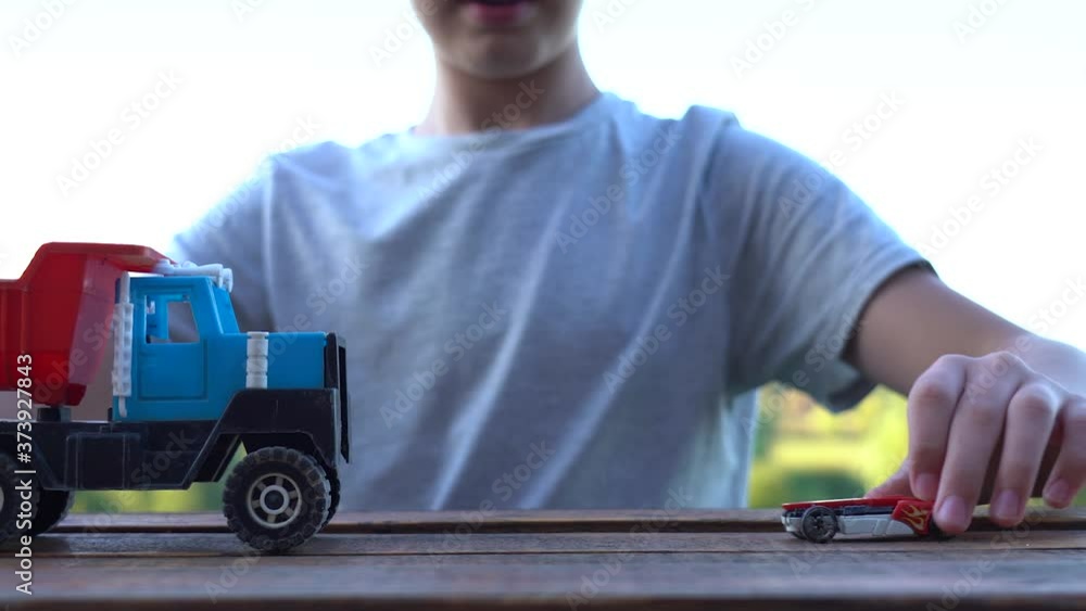 Kid playing with small toy car and big plastic lorry on wooden vintage background. Closeup view video of boy hands hold two transport toys with both hands and attack and crash them. Kid playing with small toy car and big plastic lorry on wooden vintage background. Closeup view video of boy hands hold two transport toys with both hands and attack and crash them.