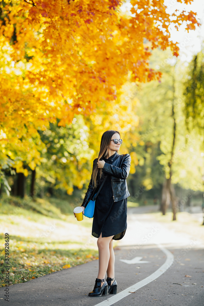 Obraz premium Young woman in stylish clothes walking in the autumn city street and drinking take away coffee in paper cup. Breakfast on the go..