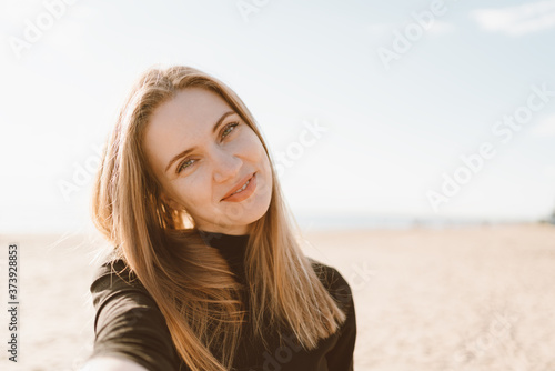 Quadro em tela Pretty female with long hair takes selfie on smartphone on beach in summer or autumn