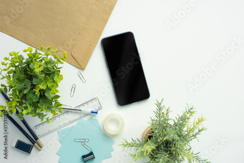 Top view of white office desk with office supplies, plants and a smartphone