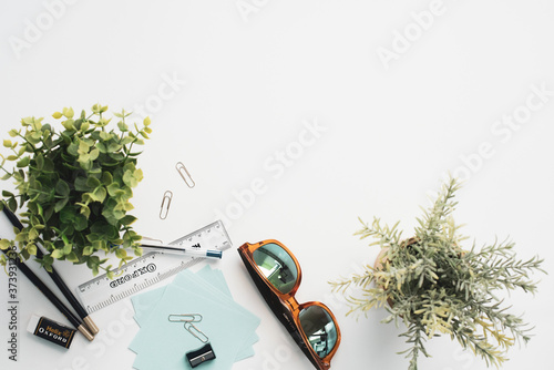 Top view of white office desk with office supplies, plants and sunglasses