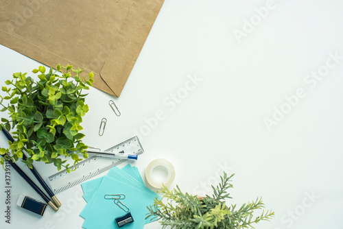 Top view of white office desk with office supplies and plants