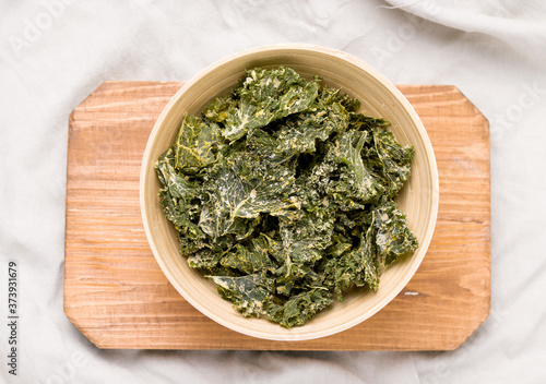 Kale chips in bowl on wooden board top view