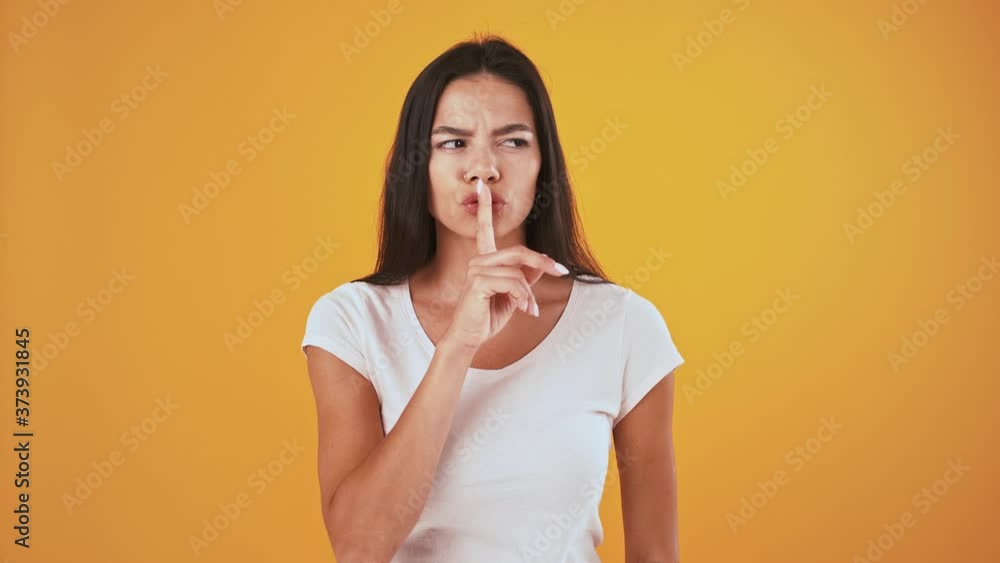 Serious female looking around, showing be quiet sign. Posing on orange background Serious female looking around, showing be quiet sign. Posing on orange background