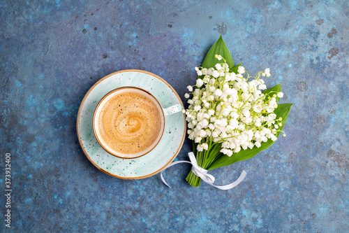 Lily of the valley flowers bouquet and coffee cup on blue background. Breakfast, morning coffee, greeting card concept. Top view, flat lay