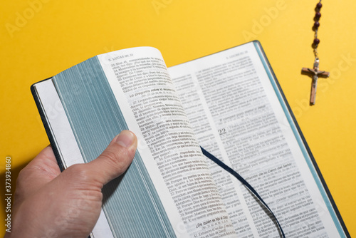 Man hand opening blurred Bible and rosary over yellow. Plain background copy space for catechism class schedule