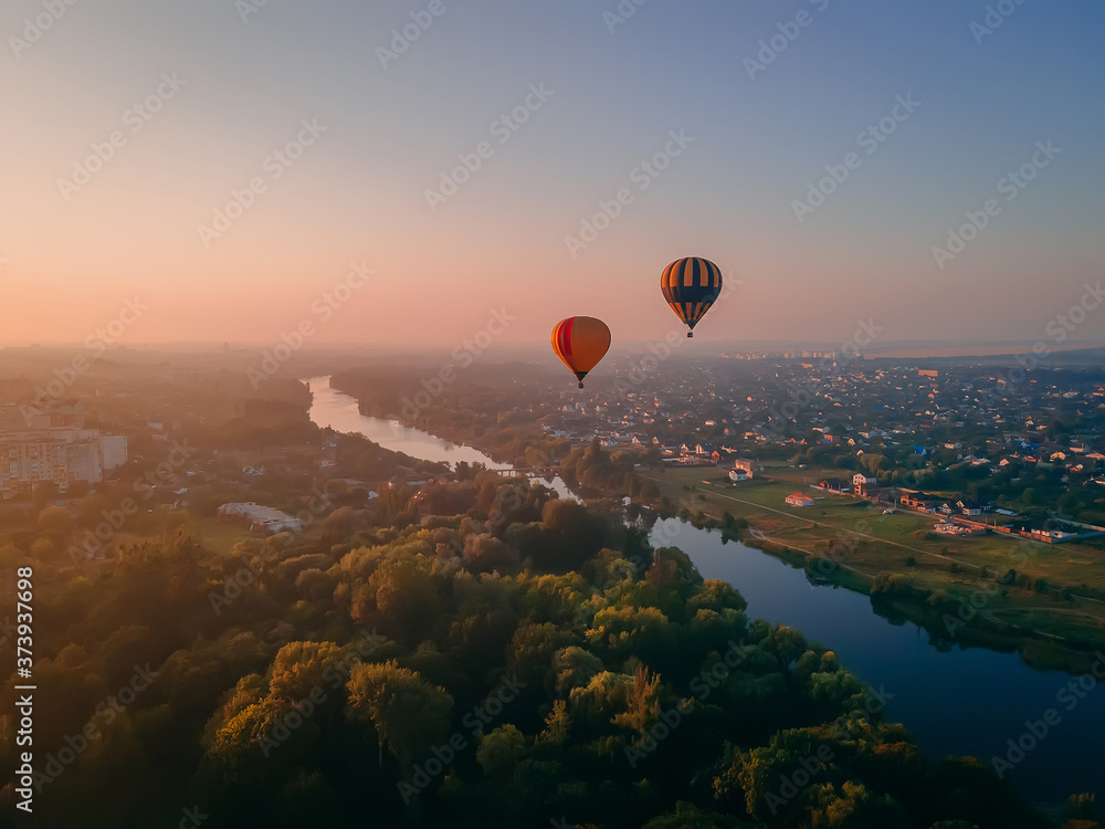 Two colorful air balloons flying over green park and river in small european city at summer sunrise